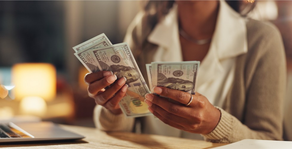 A woman displaying money in front of a laptop, indicating engagement in online financial activities.