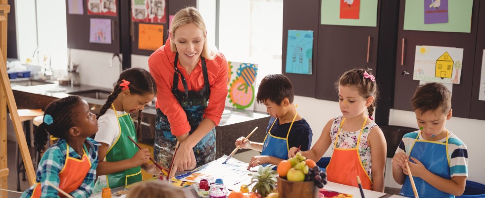 A teacher guides children in a painting class, encouraging creativity and artistic expression among young learners.
