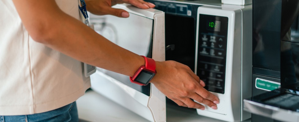 An individual is in the process of opening a microwave oven, ready to take out food that has been heated.