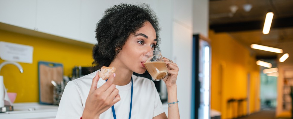 A woman sits at a table, sipping coffee and indulging in a sweet donut, creating a moment of relaxation.