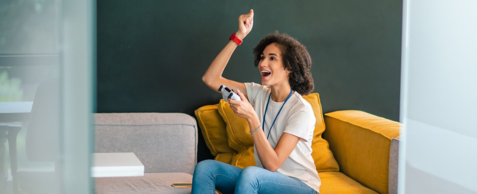 A woman sitting on a couch holding a video game controller, raising her arms in a relaxed and joyful manner, enjoying her surroundings.