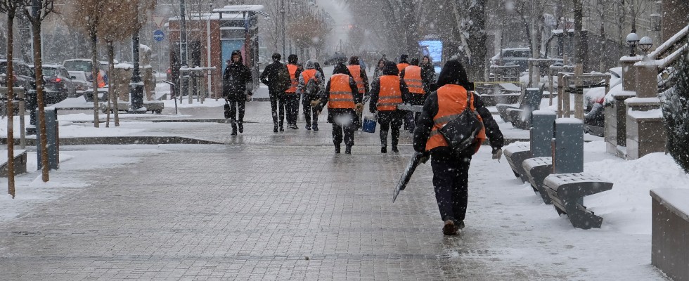 A group of people wearing orange safety vests navigate a snowy sidewalk.