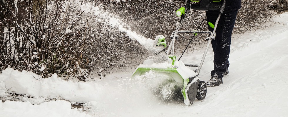 A person operates a snow blower, efficiently clearing a path through freshly fallen snow in a winter landscape.