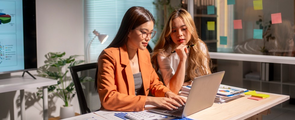 Two women collaborating at a desk, focused on a laptop, engaged in a productive discussion.