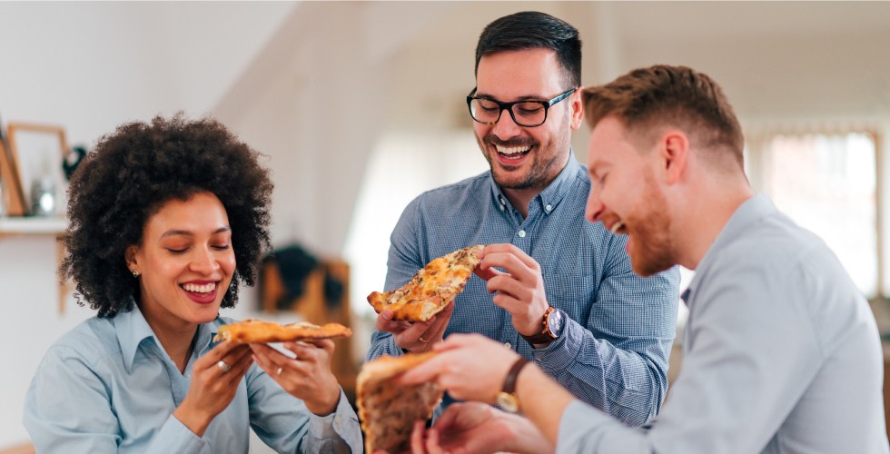Three friends enjoying pizza together at a work meeting.