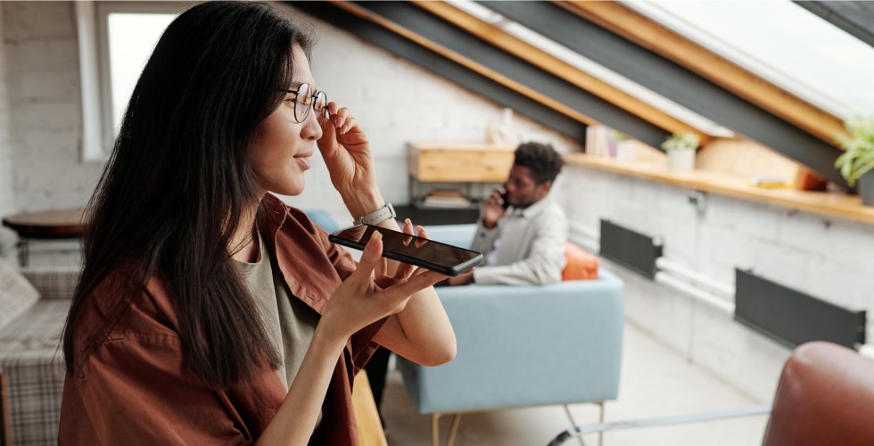 A woman adjusts her glasses while speaking into a smartphone.