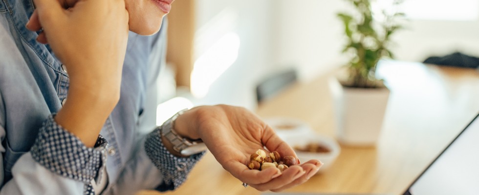 A woman sitting at a desk with a laptop, holding a handful of nuts for snacking.