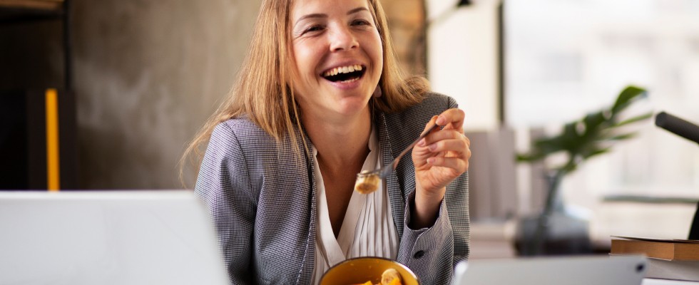 A woman joyfully eats fruit, her laughter evident.