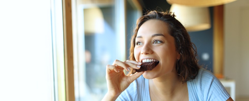A woman enjoying a chocolate bar, smiling as she takes a bite, savoring the sweet treat.