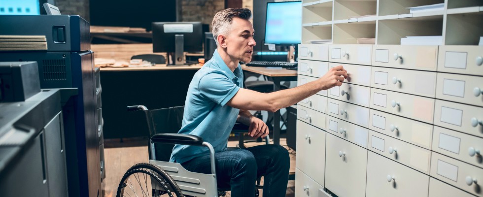 A worker moves to open a drawer on a large filing cabinet in a cozy office space.