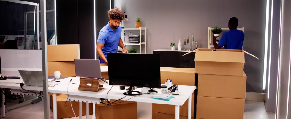Two workers unpack and assemble an office space, including laptops, monitors, and decor.