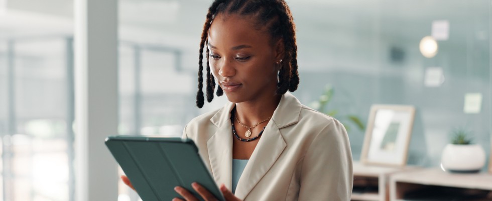 A woman in a business suit is focused on using a tablet in a professional setting.