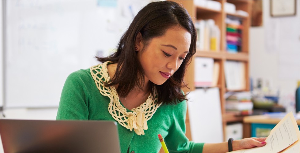 A woman seated at a desk, focused on her laptop, surrounded by a tidy workspace.