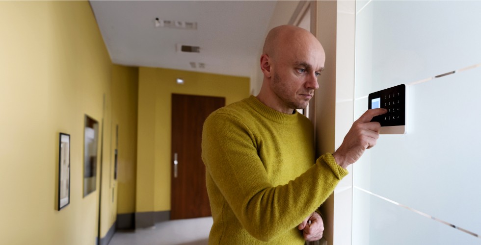 A man interacts with a security system control panel on a wall, typing in a secret and secure code.