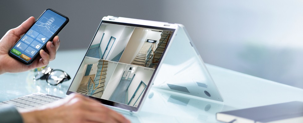 A person is focused on a security camera feed, using both a laptop and a smartphone.