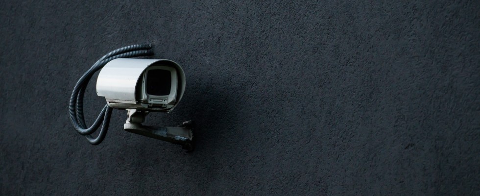 A security camera is securely mounted on a black wall.