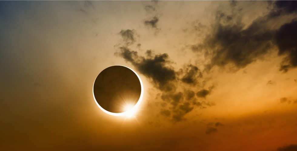 The circle shape of the moon is shown in front of the glowing sun illustrating a solar eclipse against a dark sky with a few cloud.
