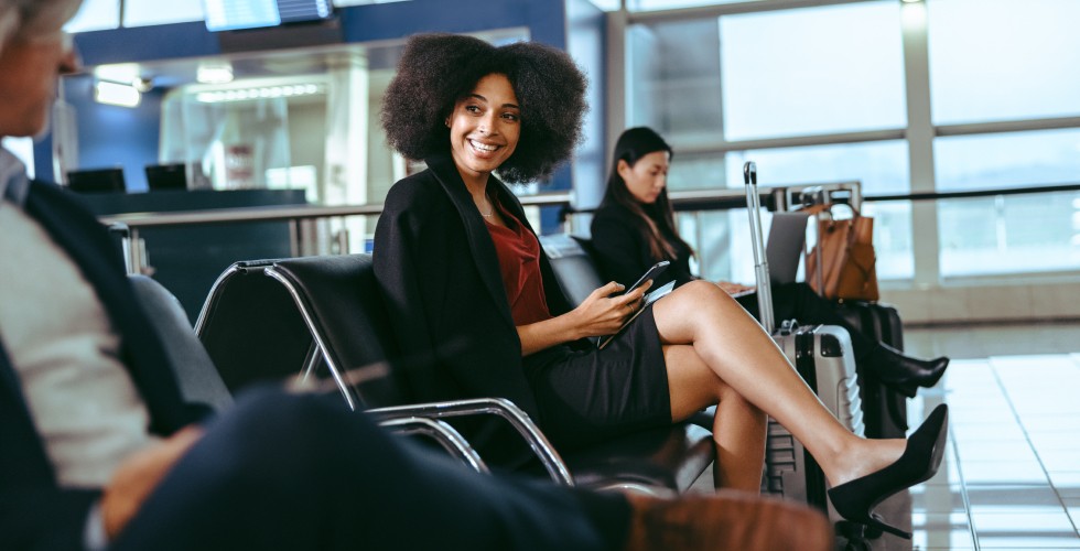 A woman sitting on a chair in an airport terminal, waiting with her luggage beside her.