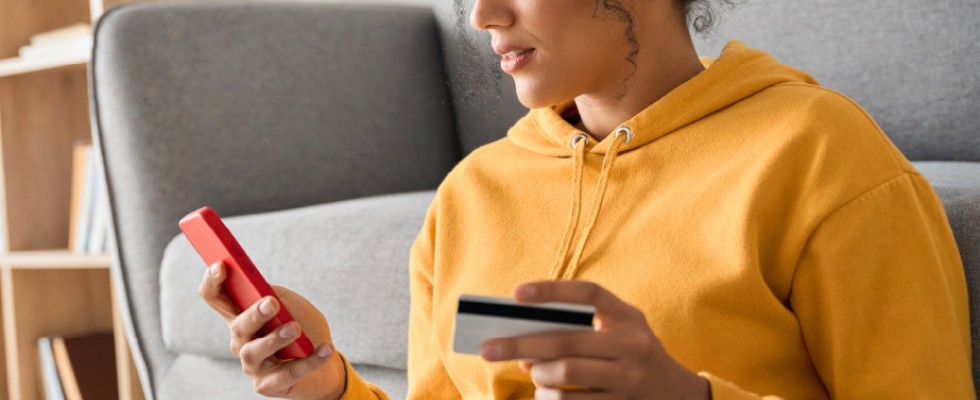 A woman is holding a credit card in one hand and a smartphone in the other, appearing engaged in a transaction.