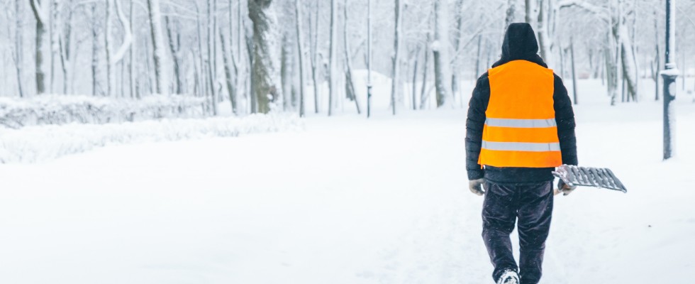 A figure in an orange vest strolls across a snowy terrain, surrounded by a serene winter atmosphere.