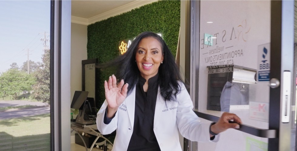 Astre Wellness founder Tonya Millions Fitch smiles and waves hello while opening the door to her business.