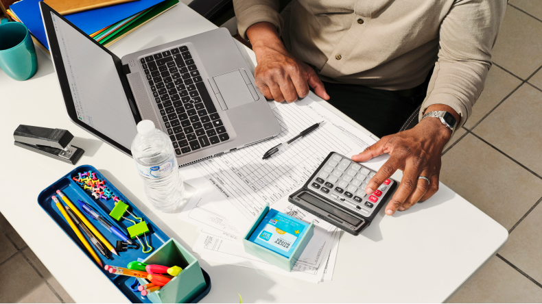 A person at an office desk, focused on a laptop and a calculator for their tasks.