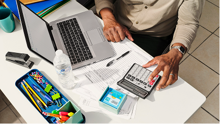 A person at an office desk, focused on a laptop and a calculator for their tasks.