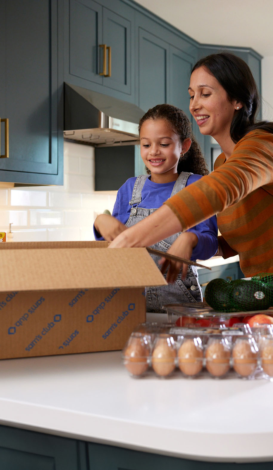 A mother and child unpack a box in the kitchen.