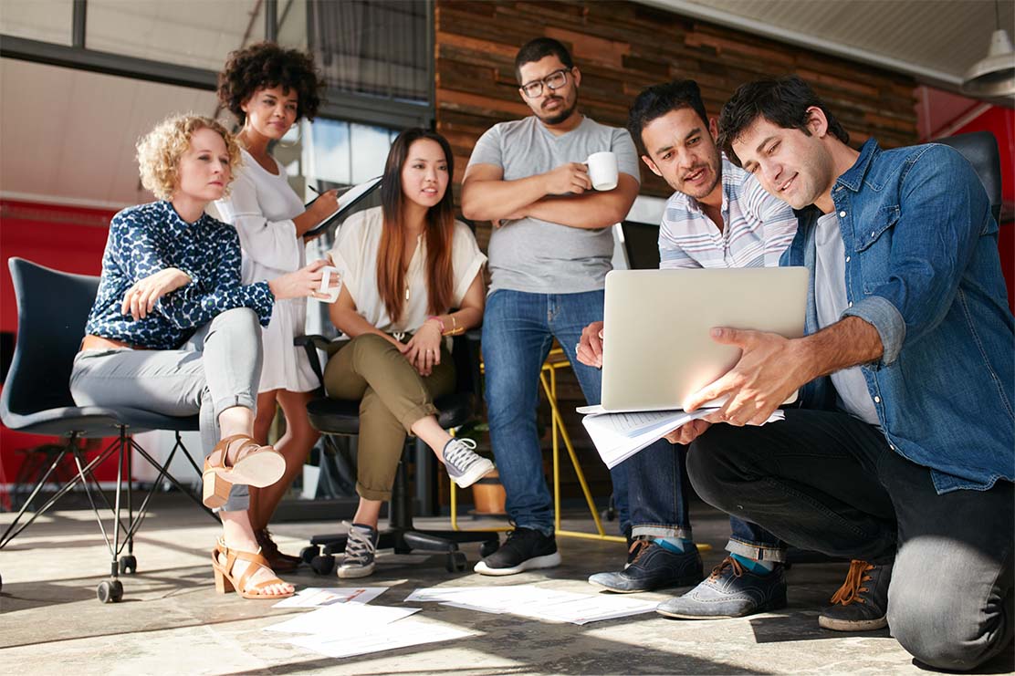 A group of diverse business people gather around a laptop.