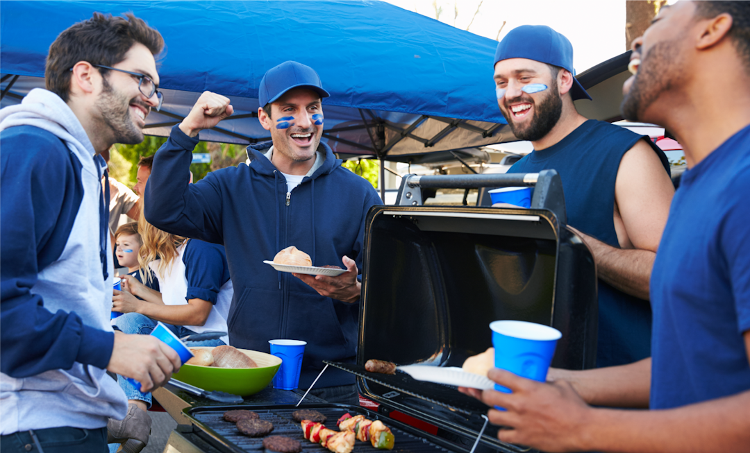 A group of men enjoying a lively barbecue at a tailgate party, laughing and sharing food in a cheerful outdoor setting.