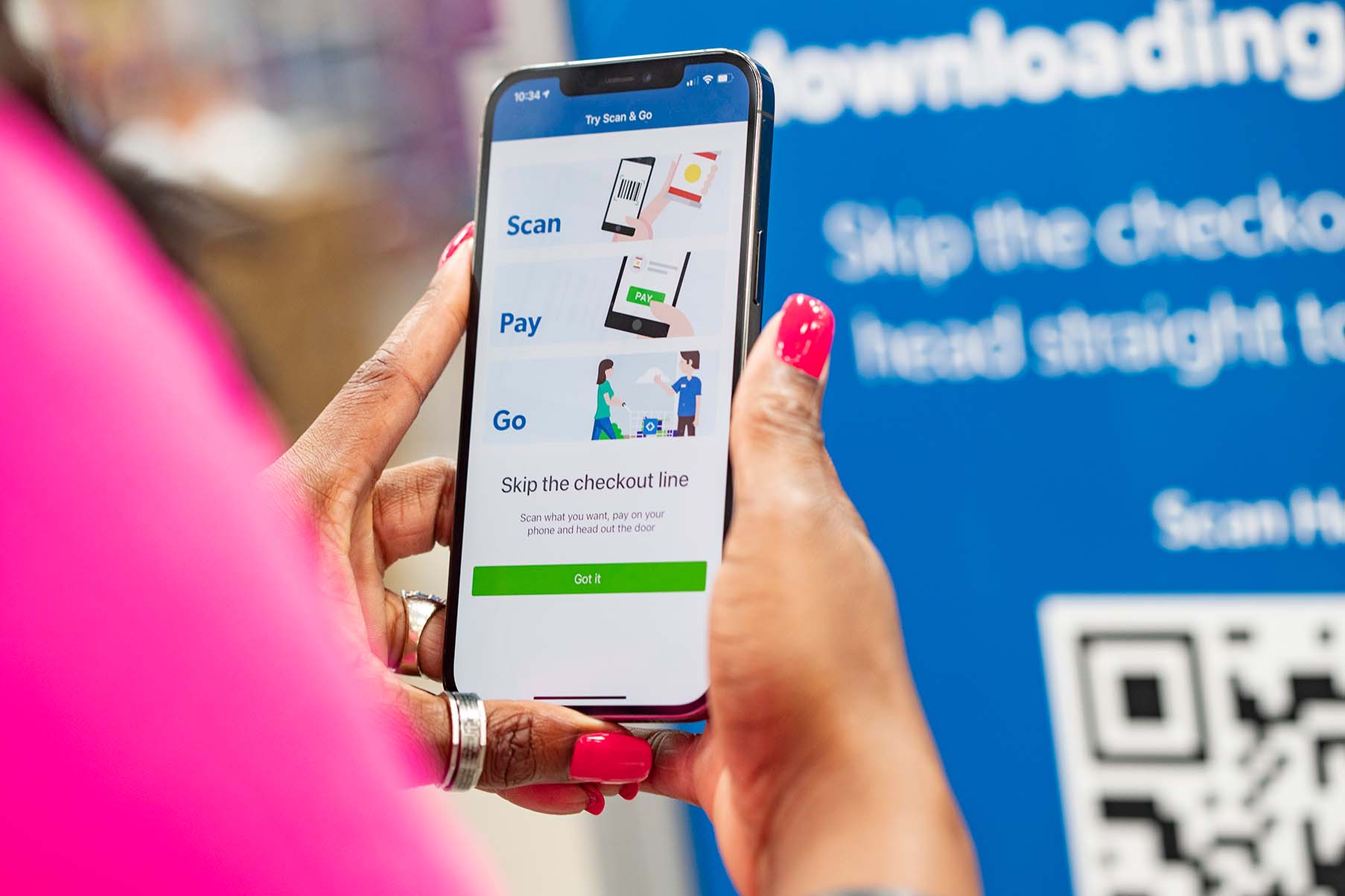 Photo of a customer holding a mobile device.  The customer is going to skip the checkout line by using Scan & Go technology.