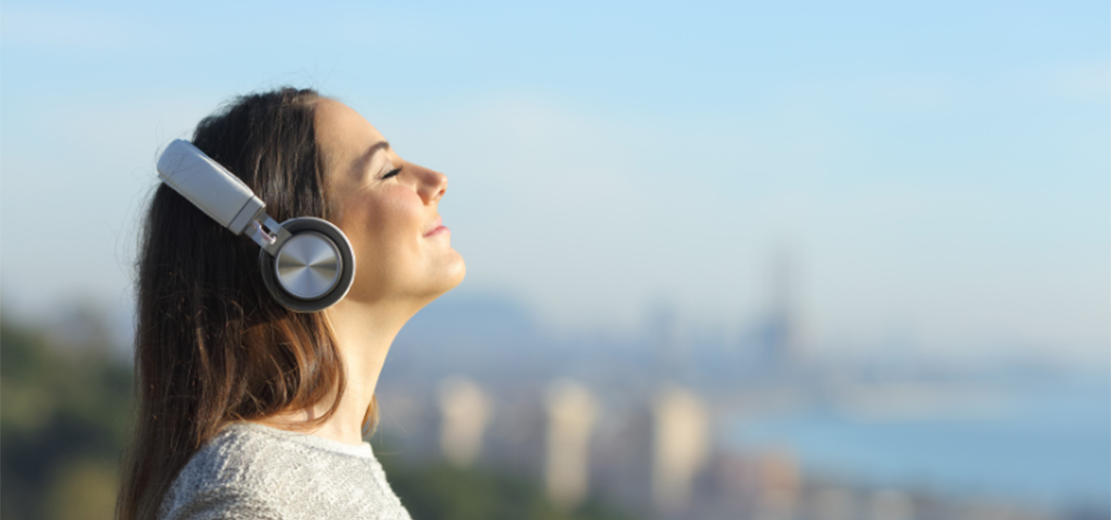 A woman wearing headphones stands outside. Her head is upturned to the sun, her eyes are closed and she has a smile on her face. She's listening to the Sounds of Summer countdown from Walmart Radio!