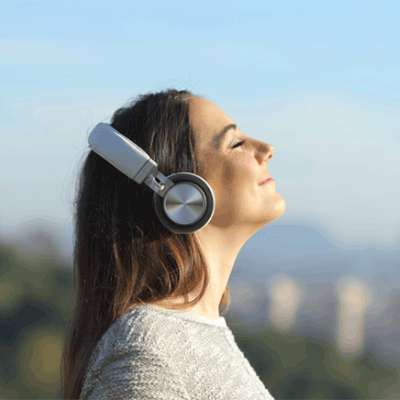 A woman wearing headphones stands outside. Her head is upturned to the sun, her eyes are closed and she has a smile on her face. She's listening to the Sounds of Summer countdown from Walmart Radio!