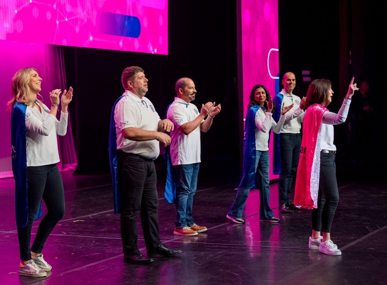 International associates wearing superhero capes on stage at the International Associates Meeting