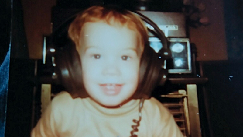 Bo Woloszyn as a toddler wearing headphones. He has an adorable smile showing about four teeth. An early premonition of his future career!